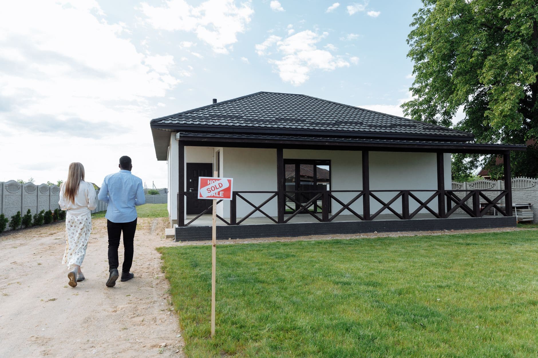 A couple walking up the path toward their newly purchased home, a Sold sign on the lawn
