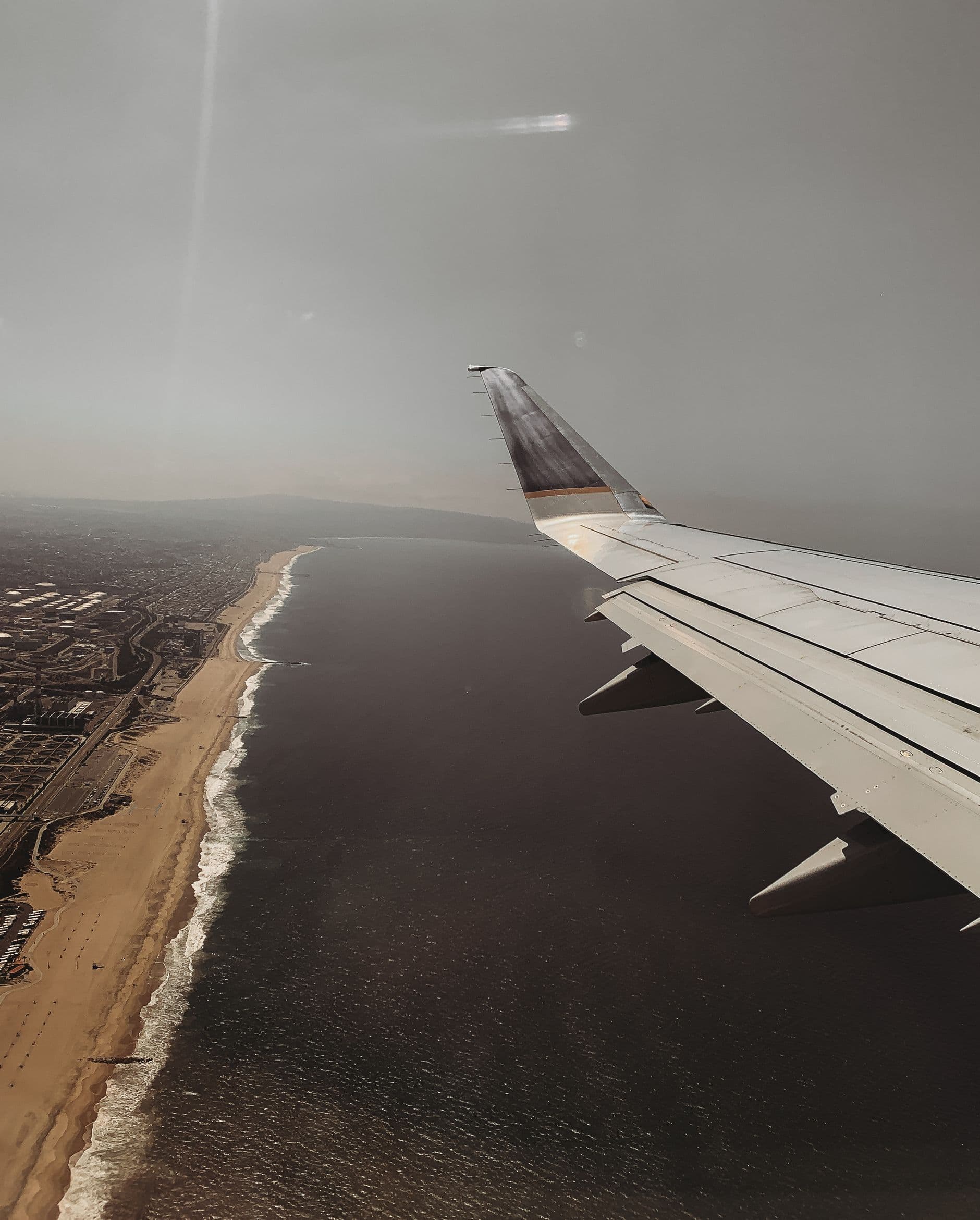View from an airplane window of a wing over a coastline, ocean on one side