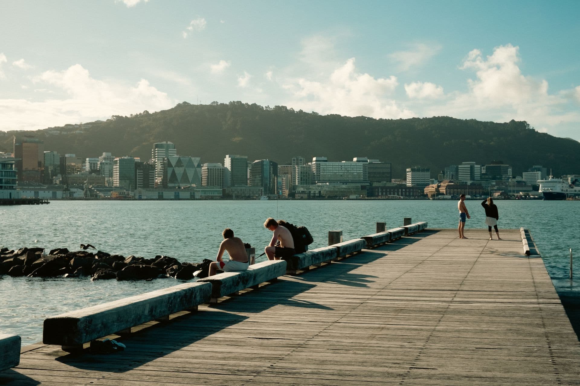 People enjoying a sunny day on Wellington's waterfront pier, with the city skyline behind