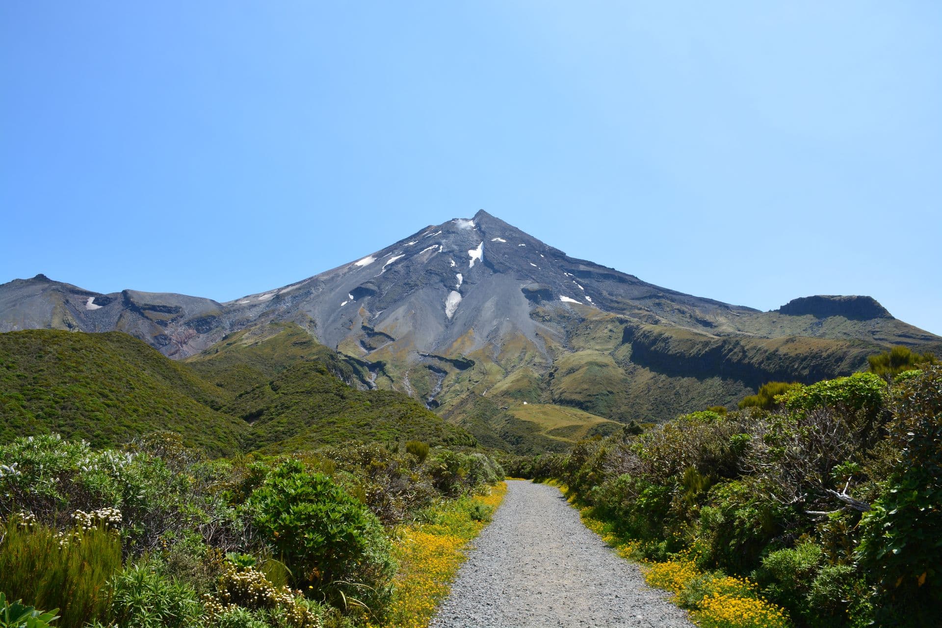 A gravel walking track through native bush toward Mount Taranaki under a clear blue sky, New Zealand
