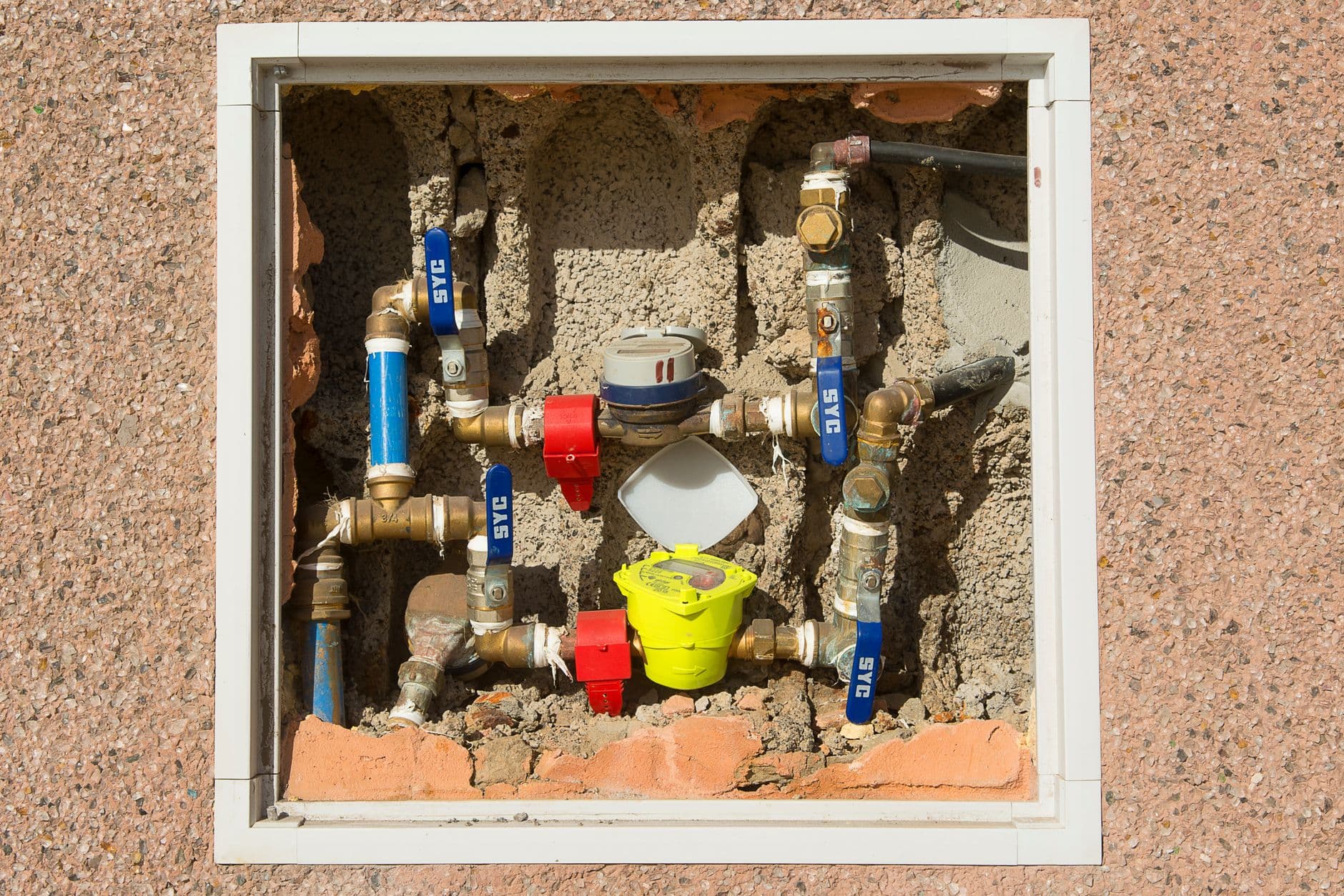 A close-up of a water meter set into a concrete wall