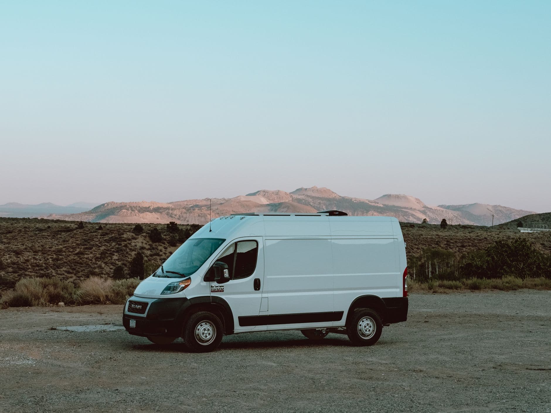 A white cargo van parked on a remote road against a mountain backdrop at dusk