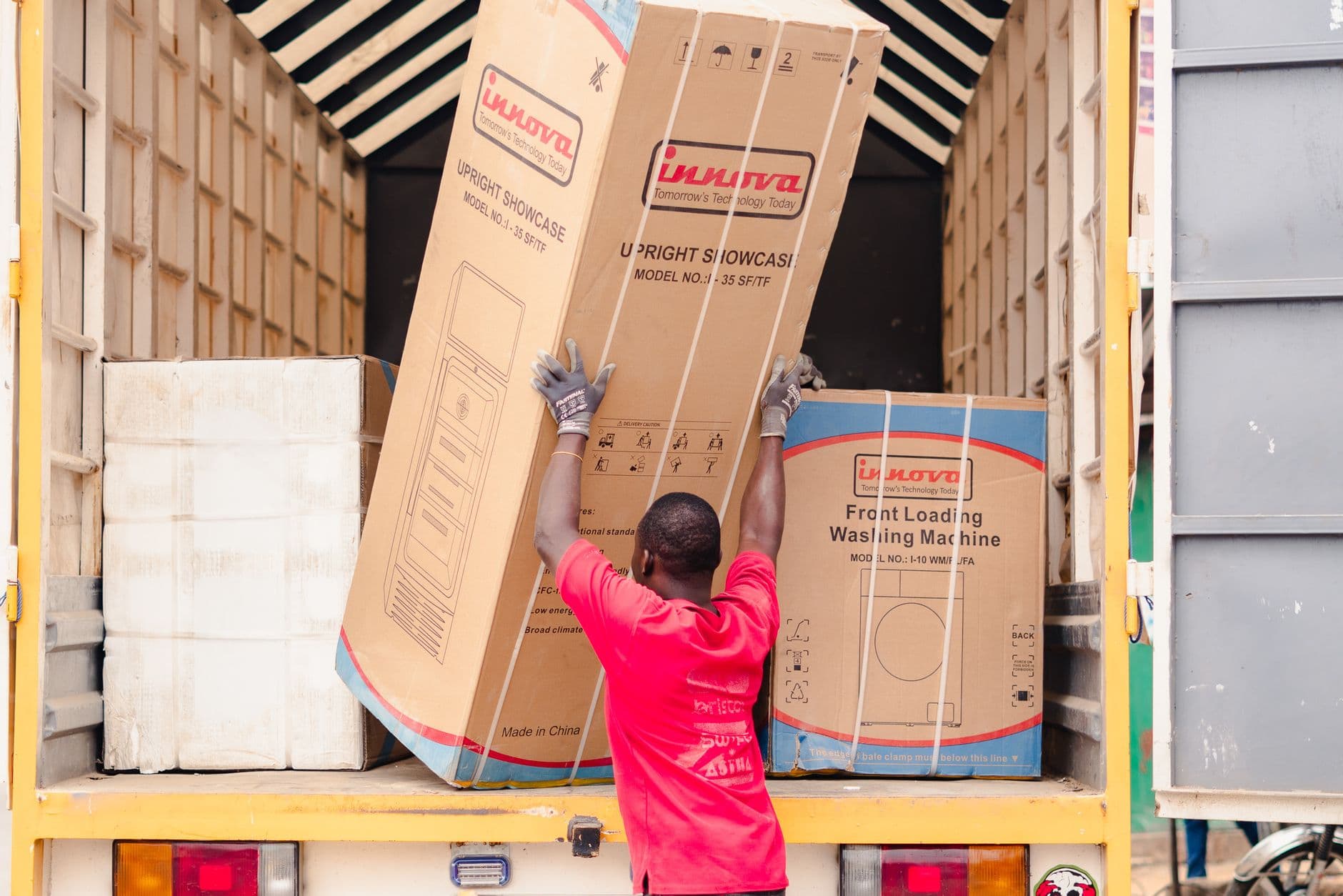 A removalist in a red shirt loading a boxed appliance onto a truck