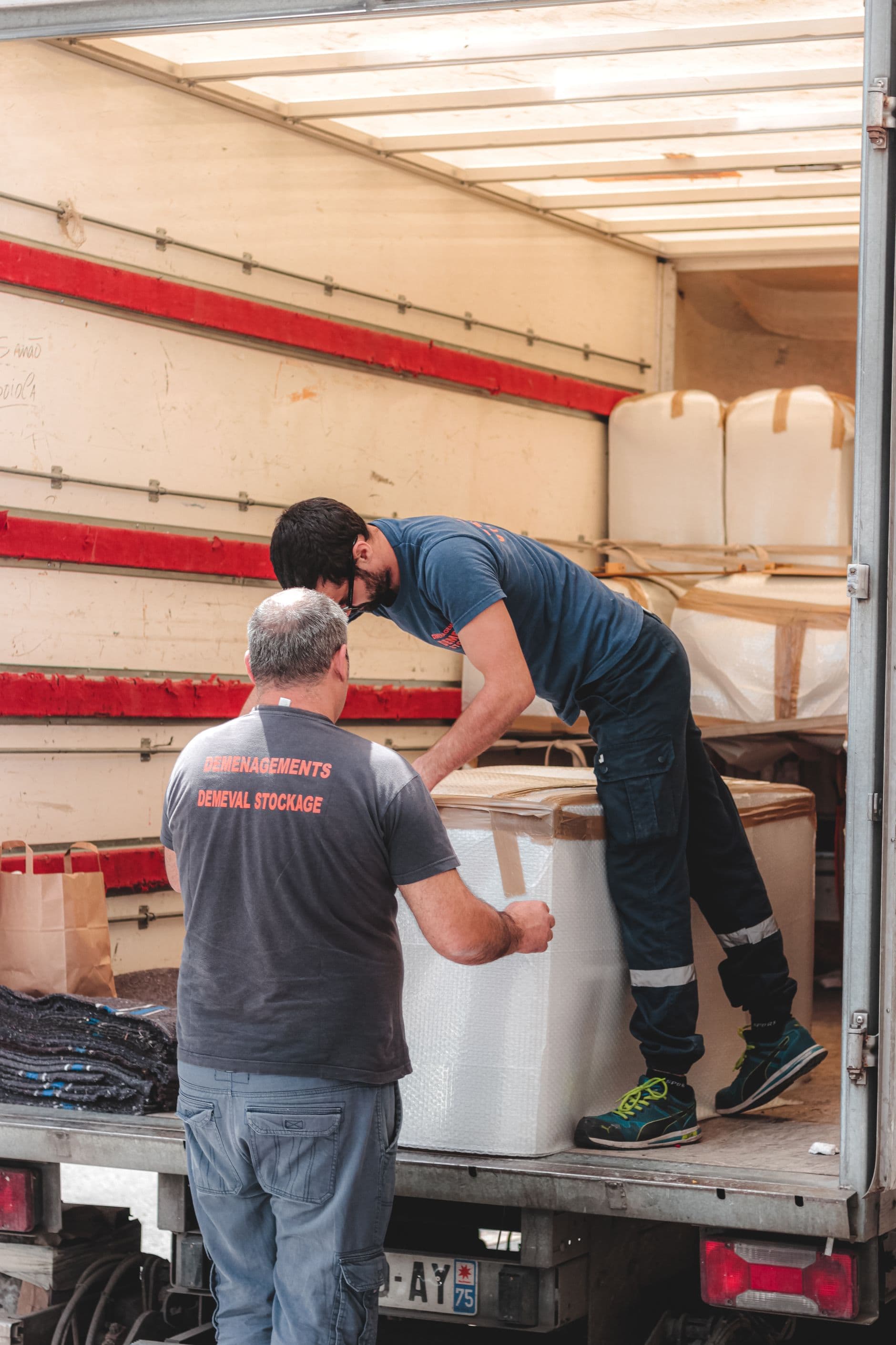 Two removalists loading a large box into the back of a moving truck
